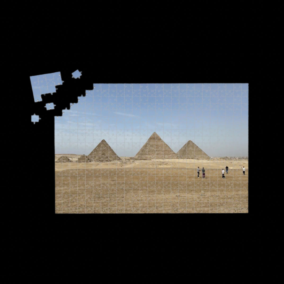 Full color image of the Pyramids of Giza under a blue sky with desert foreground and people in the distance.