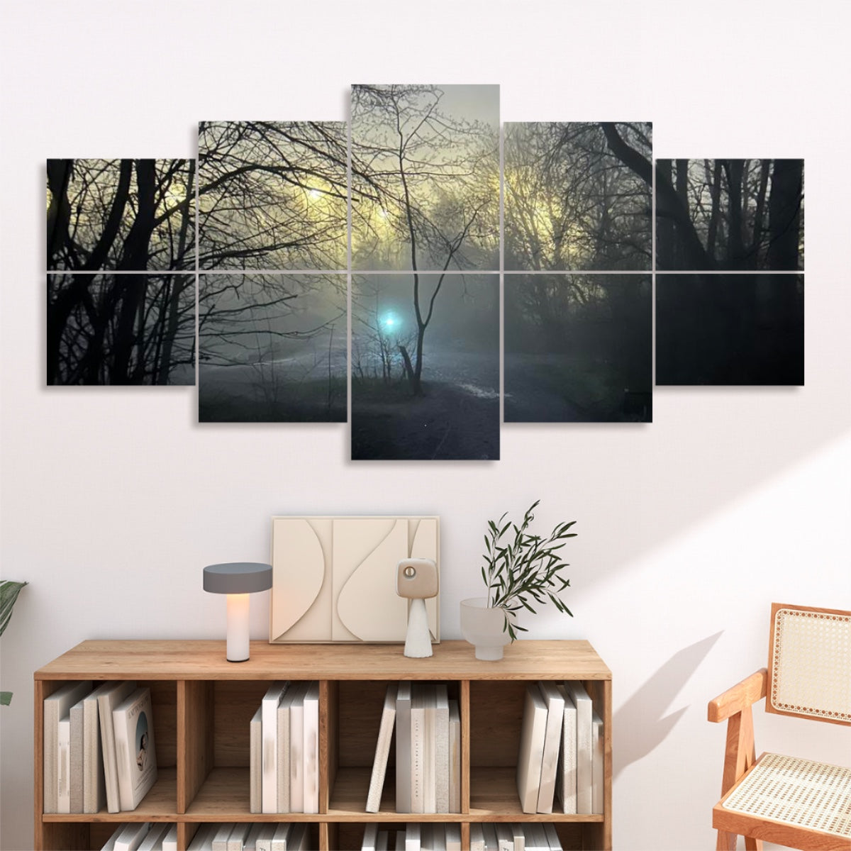 In a softly lit lounge, all ten panels hang above a low wooden console. The misty-forest image spans a warm white wall, drawing the eye to the glowing teal orb nestled among the trees. Below, a simple console holds neutral-toned decor, and a wicker chair sits at the left, framing the installation