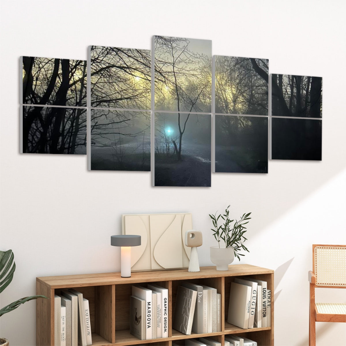 Viewed from a corner angle, the “Light” panels hover over a minimalist console topped with a lamp and vases. Golden morning light filters through bare branches in the artwork, while the teal orb glows above a fog-laden path. To the right, a cane-armchair completes the tranquil setting