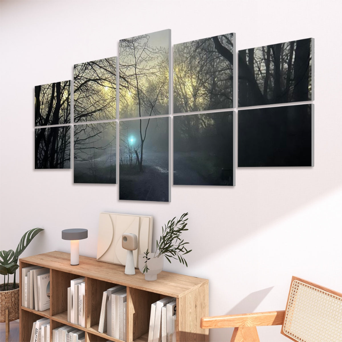 Viewed from a corner angle, the “Light” panels hover over a minimalist console topped with a lamp and vases. Golden morning light filters through bare branches in the artwork, while the teal orb glows above a fog-laden path. To the right, a cane-armchair completes the tranquil setting