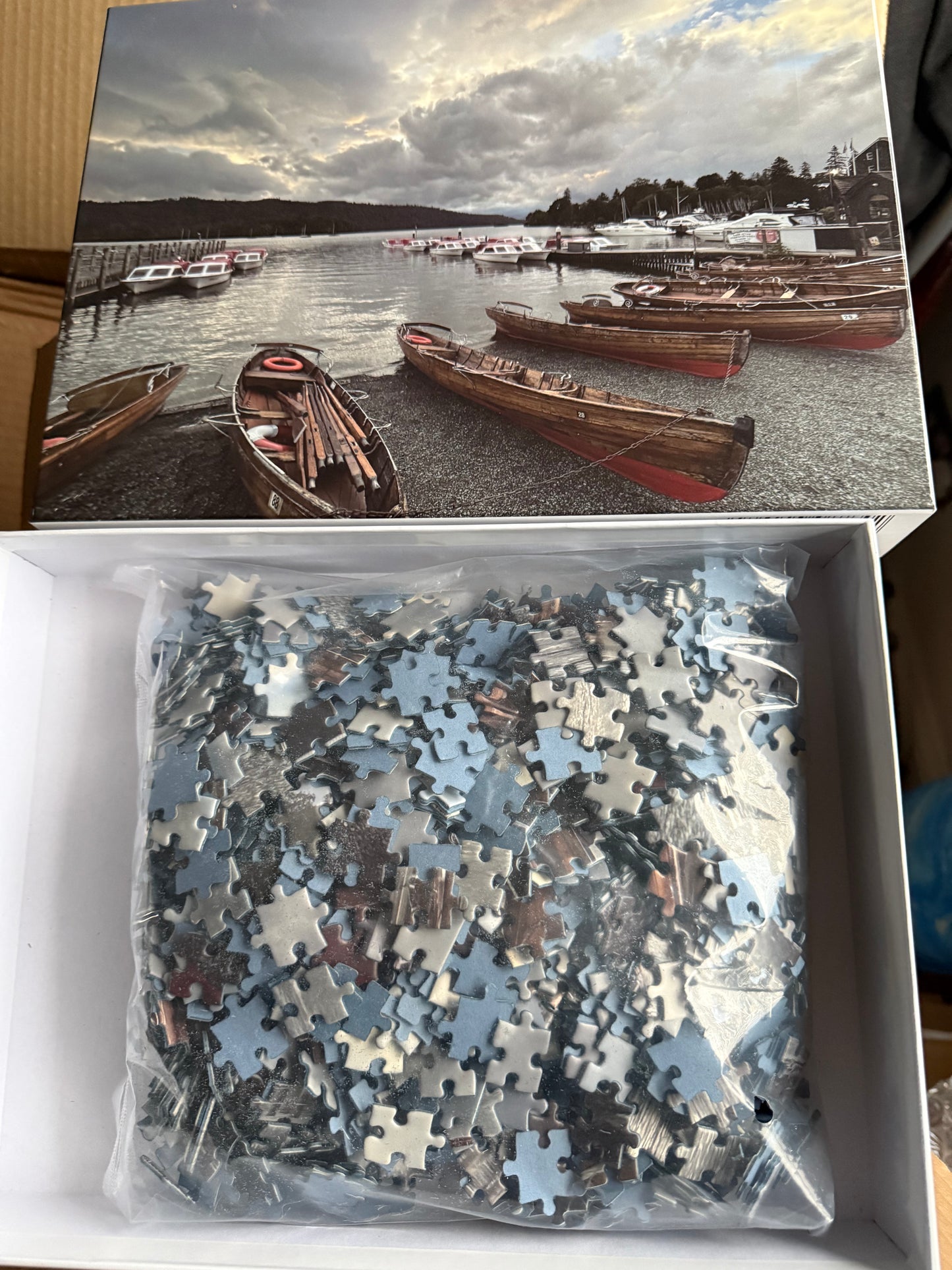 Puzzle box with a scenic image of boats on a lake and puzzle pieces inside.