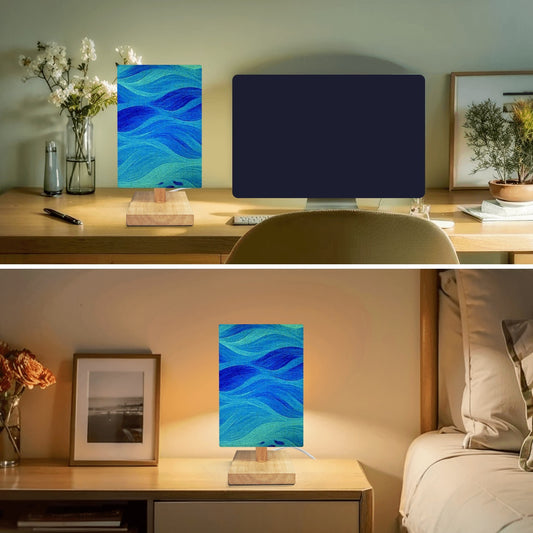 Square lamp with a linen shade in cool blue-green waves and metallic gold accents on a wooden base