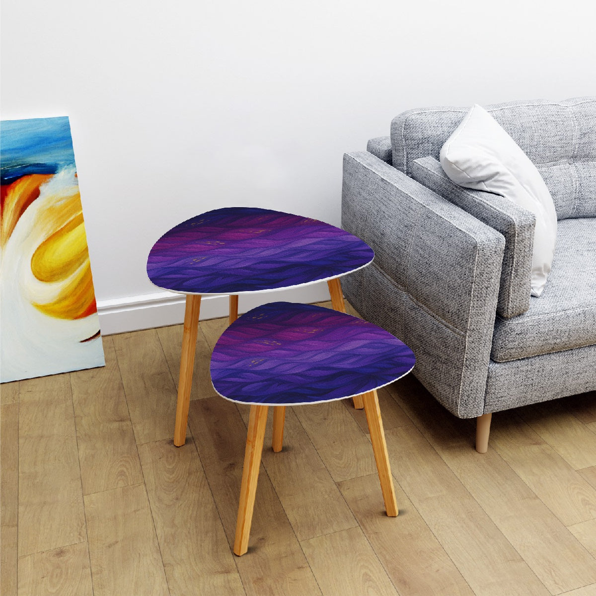 Pair of nested triangle tables with purple-gold leather tabletops arranged on a white rug in front of sheer curtains; bamboo legs rest on wood flooring
