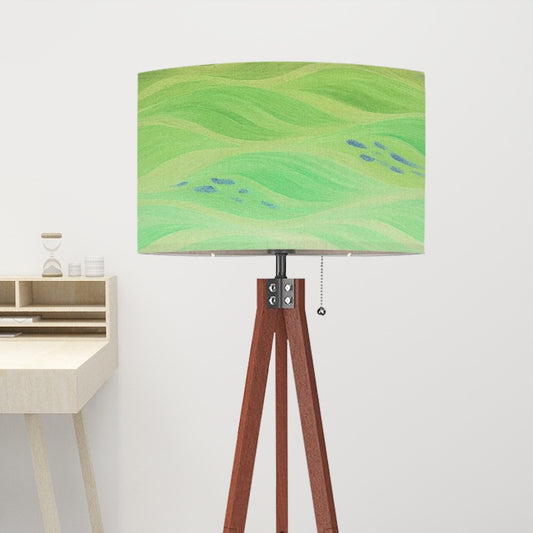 Tripod floor lamp with a linen shade displaying color-inverted green and blue currents, perched on a warm wood tripod base, evoking an avant-garde aesthetic.